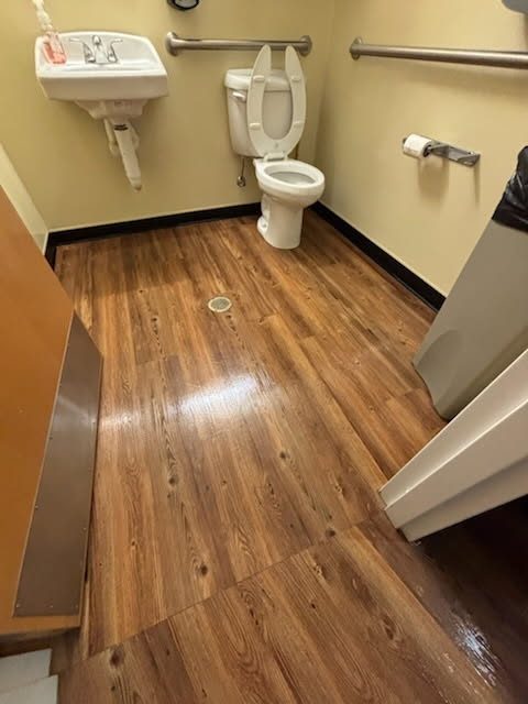 Accessible facility restroom with fixtures cleaned and wood-look floor mopped by AICS